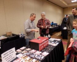 #image_title Vendor at a magic expo booth demonstrates a card trick to two men.